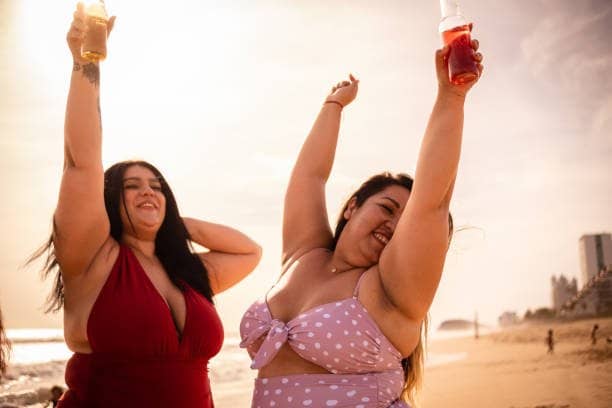 Friends drinking and celebrating on the beach wearing bikinis for fat women